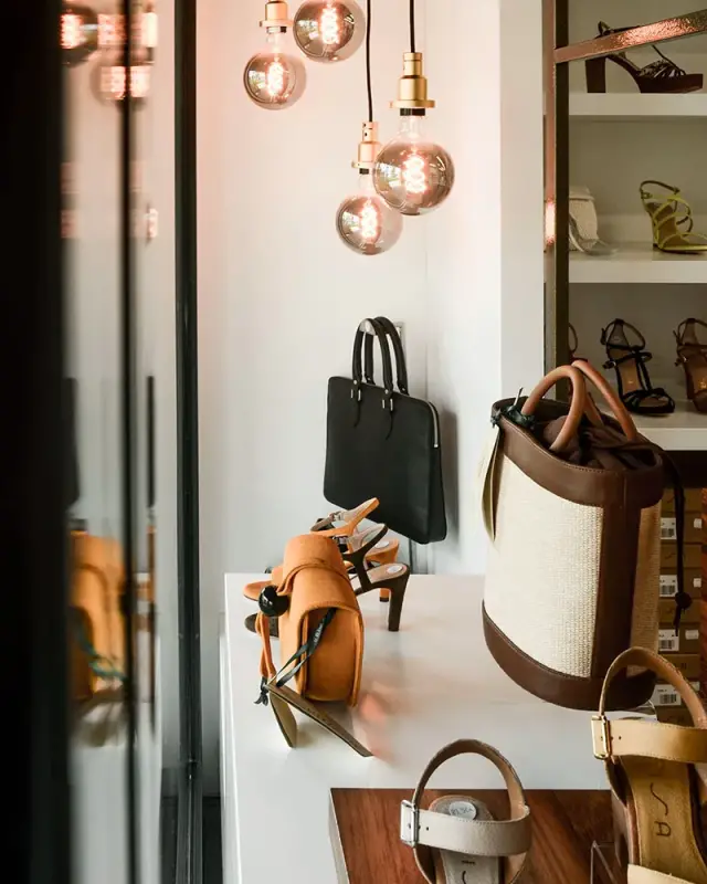 Podium blanc et bois avec sacs en cuir et toile et sandales, rayonnages en arrière-plan