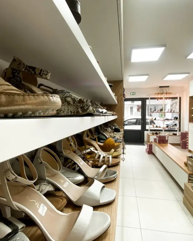 Étagères blanches profondes remplies de chaussures le long de la boutique, banc central en chêne clair