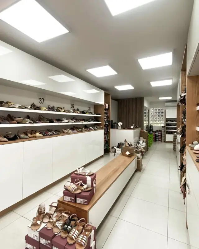 Vue vers le fond de la boutique avec rayons des pointures 35 à 38, banc en chêne et mur en tasseaux de bois