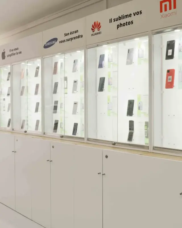 Linéaire de vitrines éclairées présentant les smartphones par marque au-dessus de meubles blancs