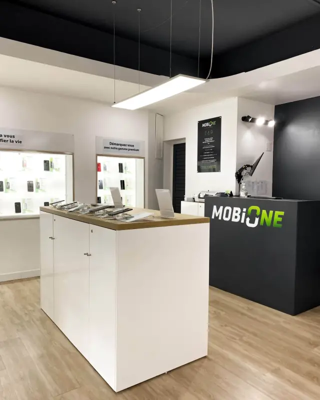 Îlot central blanc au plateau chêne présentant des smartphones sur supports sécurisés sous une suspension LED
