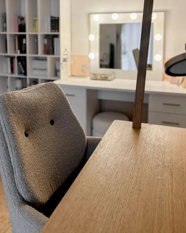 Chaise en bouclette grise devant la coiffeuse blanche aux poignées dorées