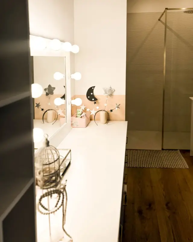 Coiffeuse blanche et miroir à ampoules, avec vue sur la douche vitrée de la salle d’eau attenante