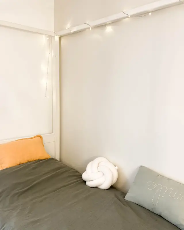 Angle du lit cabane avec guirlande lumineuse et coussins brodés