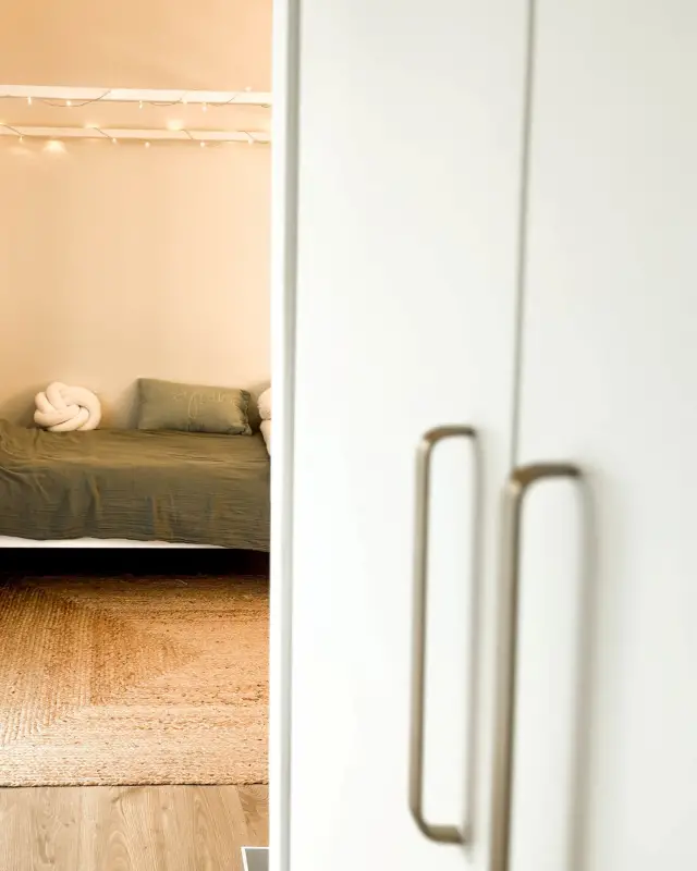 Poignées en laiton au premier plan, lit à la parure kaki et tapis en jute en arrière-plan