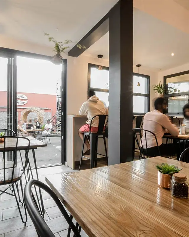 Tables en bois et chaises noires en fil métallique face aux baies ouvertes sur la terrasse