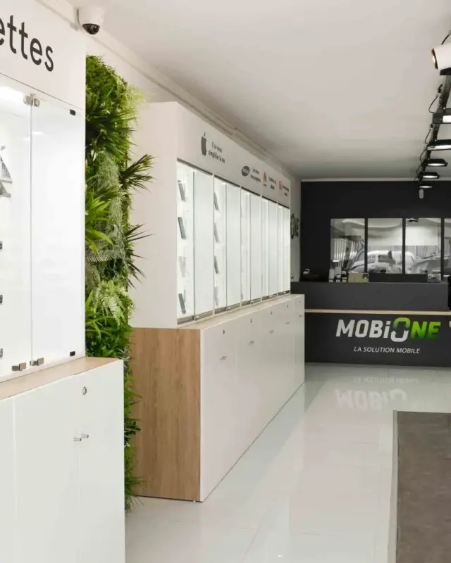 Vitrines Ordinateurs & Tablettes sur meubles bas blancs, mur végétal et tables en bois clair