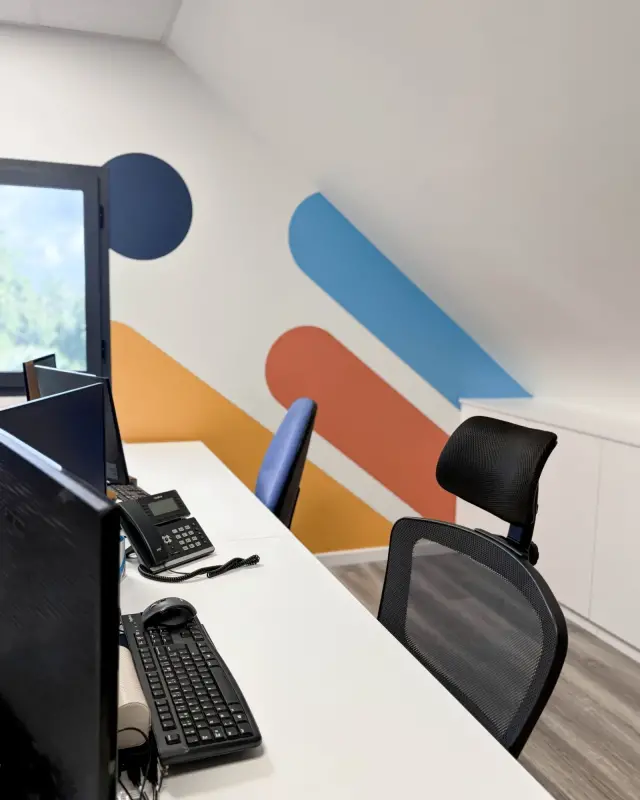 Bureau partagé avec postes blancs et fresque murale bleu marine, bleu ciel, corail et jaune sous le rampant