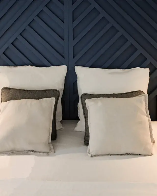 Lit blanc avec coussins gris et beige entre deux chevets en bois clair, devant la tête de lit bleu nuit