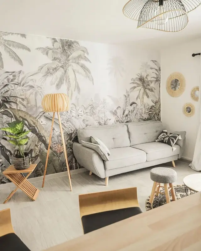 Salon d’une location saisonnière à Saint-Denis avec papier peint jungle, canapé gris et lampadaire en bois
