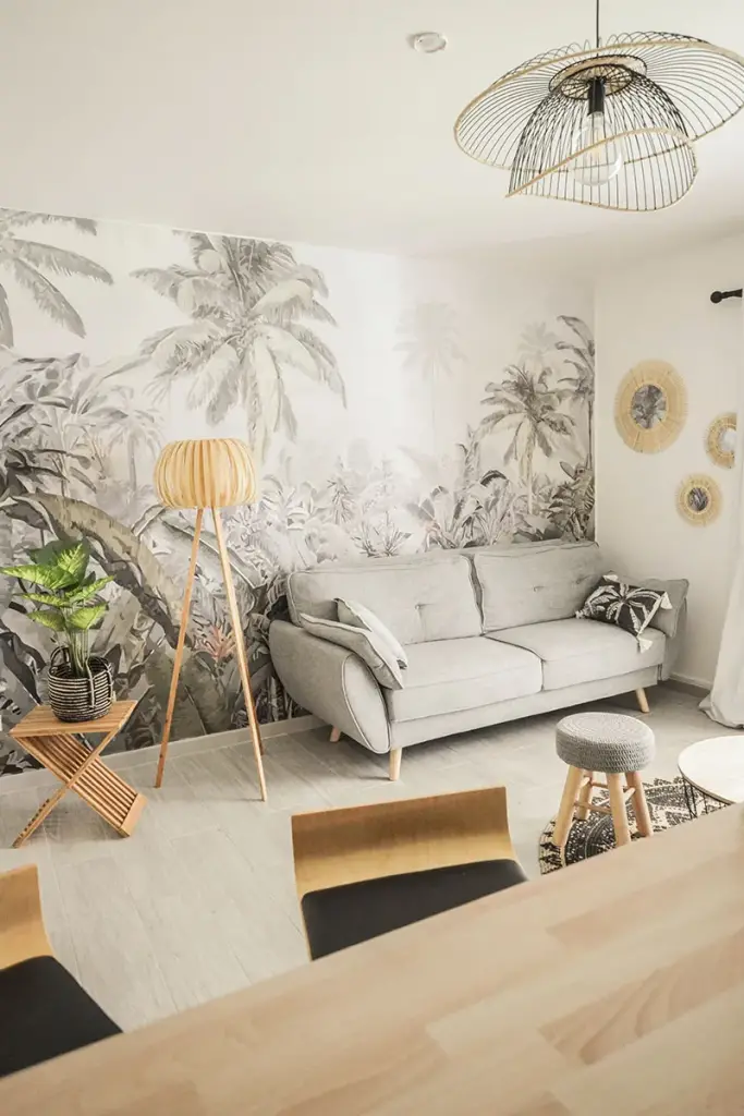 Salon d’une location saisonnière à Saint-Denis avec papier peint jungle, canapé gris et lampadaire en bois