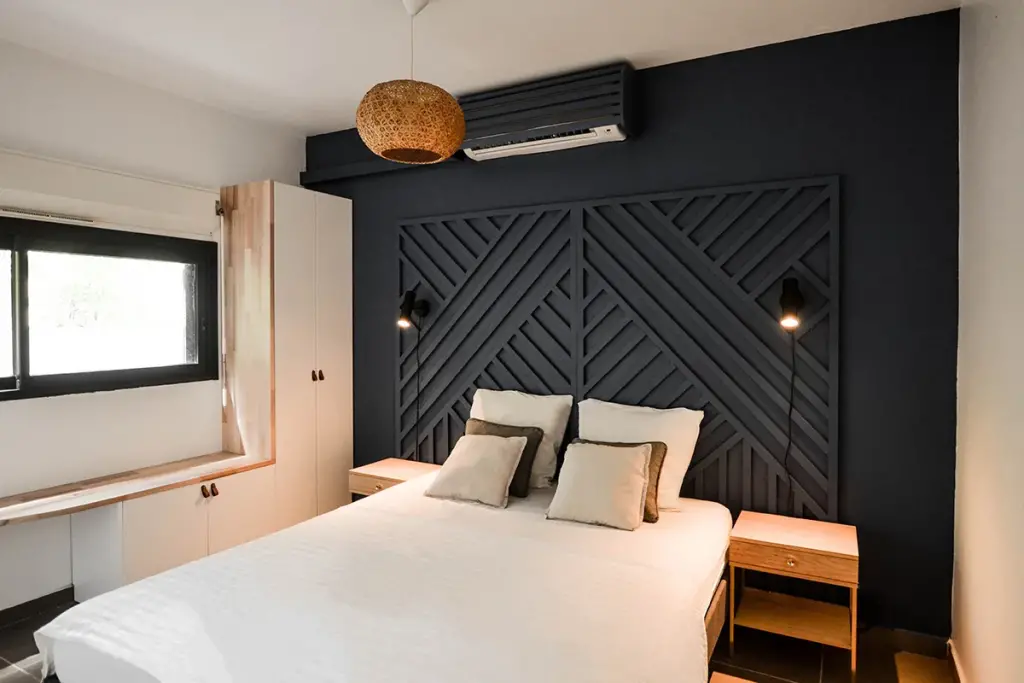 Chambre d’une location saisonnière à Saint-Gilles-les-Bains avec mur bleu nuit et tête de lit en tasseaux géométriques