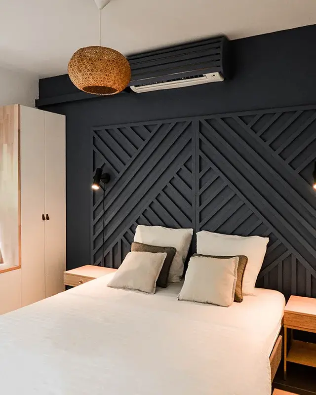 Chambre d’une location saisonnière à Saint-Gilles-les-Bains avec mur bleu nuit et tête de lit en tasseaux géométriques