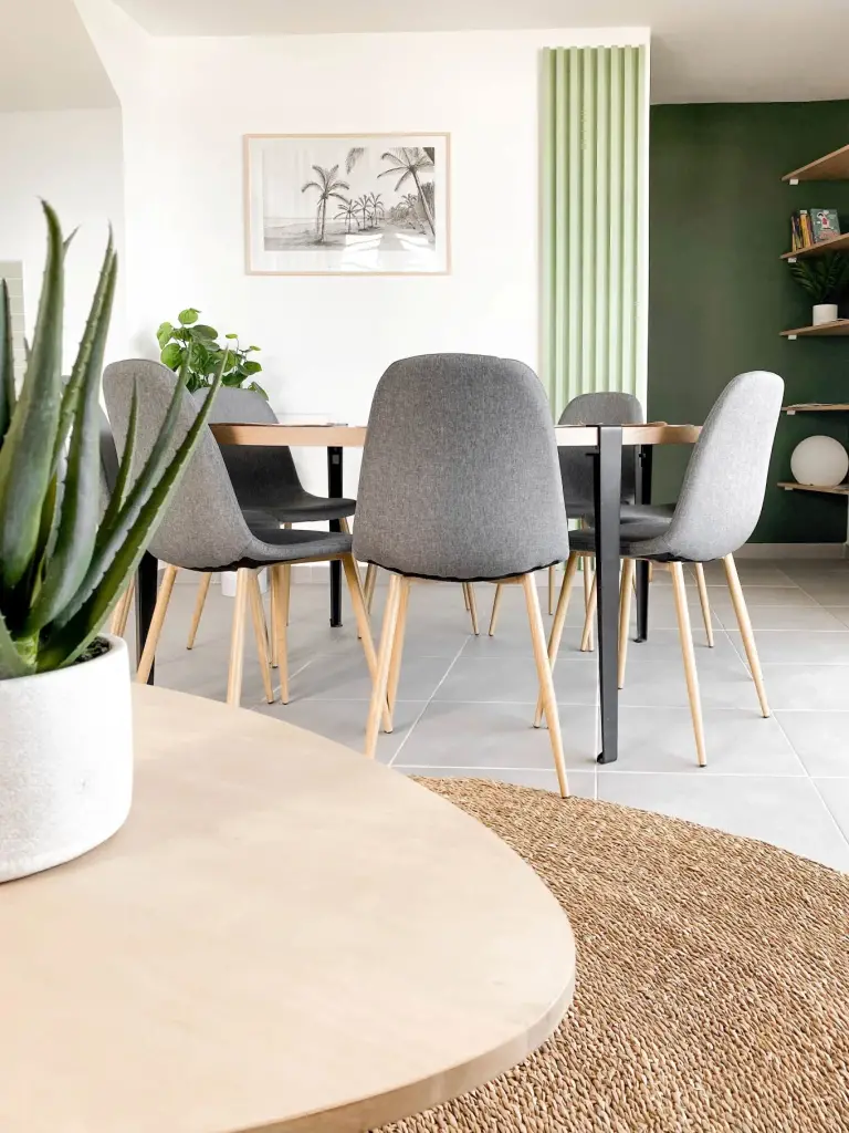 Espace repas d’une location saisonnière à Saint-Paul avec table ronde en bois, chaises grises et mur vert sapin