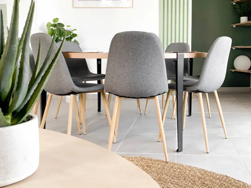 Coin repas lumineux avec table ronde en bois clair et chaises grises dans une location saisonnière à Saint-Paul