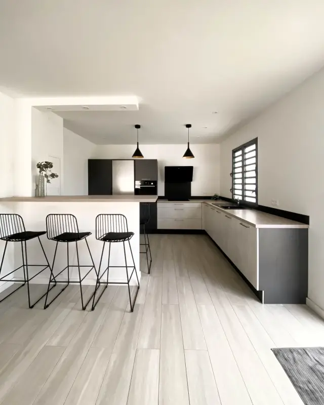 Cuisine ouverte d’une villa en location saisonnière à La Possession avec façades effet béton, bar et tabourets noirs
