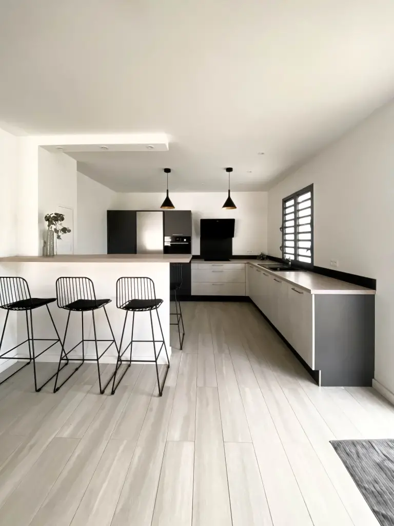 Cuisine ouverte d’une villa en location saisonnière à La Possession avec façades effet béton, bar et tabourets noirs