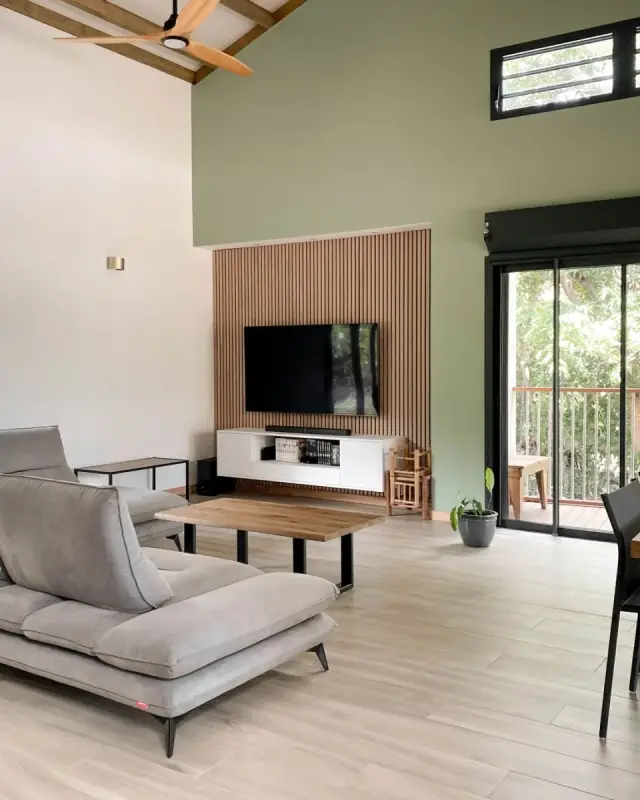 Canapé d’angle gris, table basse en bois et mur TV en tasseaux, baie vitrée ouverte sur le jardin