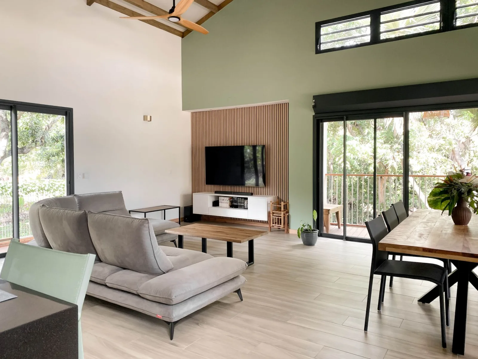 Pièce de vie décorée dans une maison neuve à L’Étang-Salé : canapé gris, mur vert sauge, meuble TV en bois et table à manger
