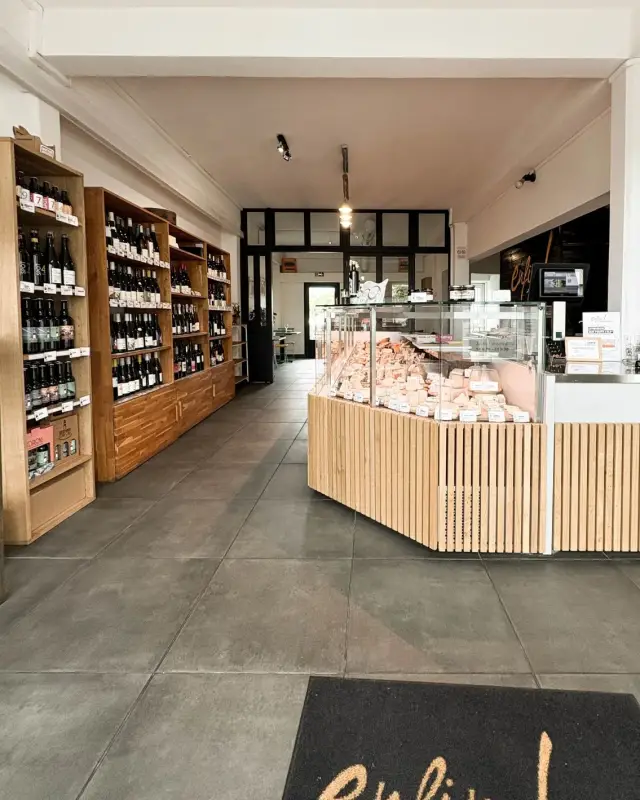 Entrée de la fromagerie avec tapis au logo de l’enseigne, vitrine de fromages et rayons de vins et de bières