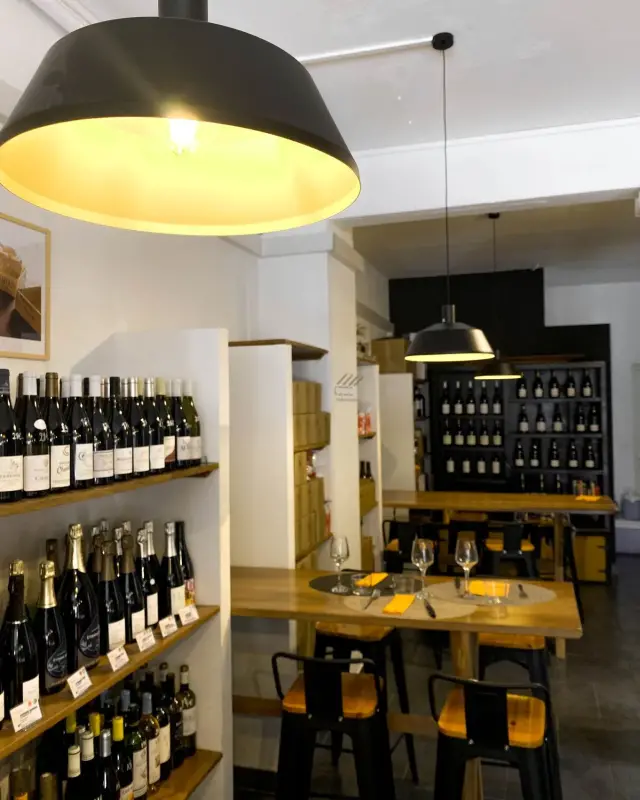 Espace de dégustation avec tables hautes en bois, tabourets noirs et suspensions cloche noires à l’intérieur jaune