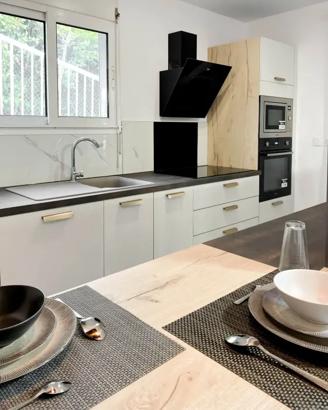 Cuisine blanche aux poignées dorées, plan effet pierre sombre, crédence effet marbre et bar en chêne dressé