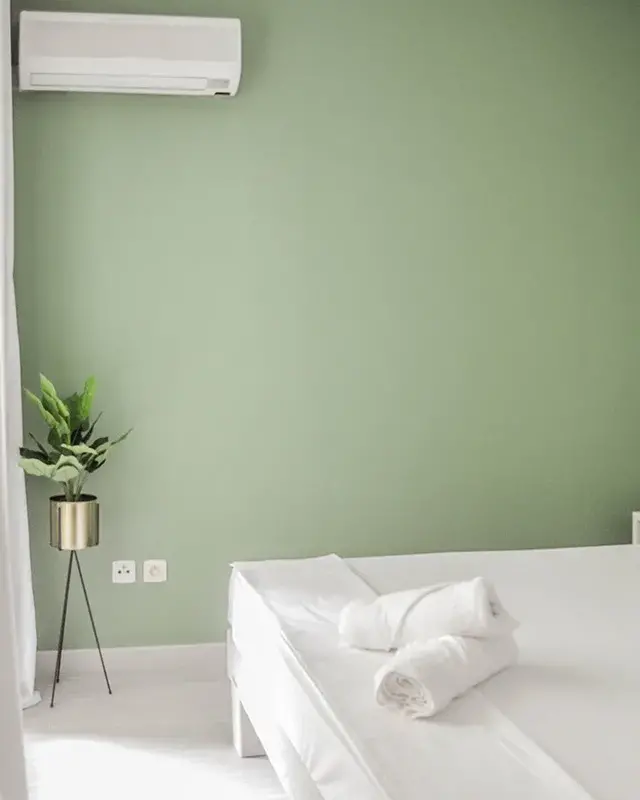 Lit blanc avec serviettes roulées devant un mur vert sauge et un lé de papier peint à feuilles de bananier