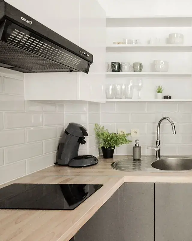 Cuisine en L avec façades grises, plan de travail effet bois, carreaux métro blancs et étagères ouvertes