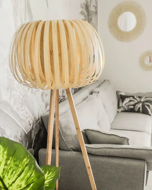 Lampadaire trépied à abat-jour en lamelles de bois devant un canapé gris et des miroirs soleil