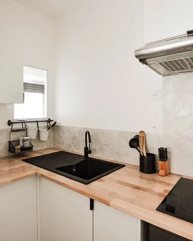 Cuisine blanche avec plan de travail en bois, évier et robinet noirs et crédence blanche en relief
