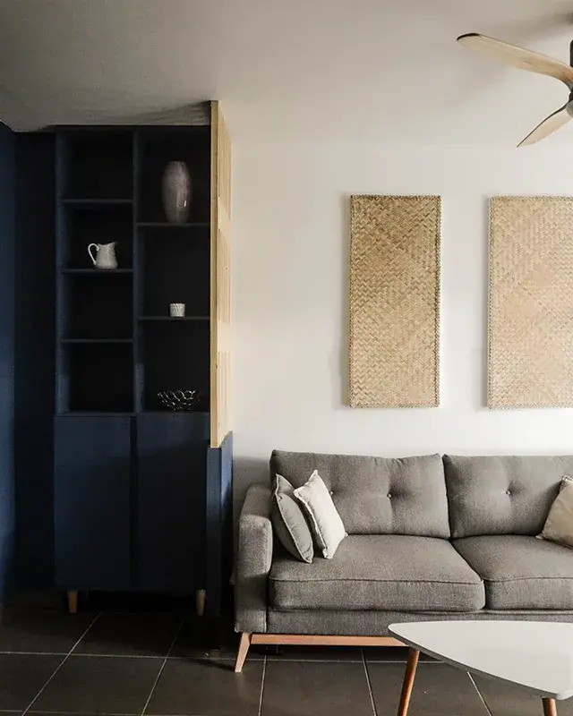 Canapé gris capitonné, tables basses blanches, panneaux en fibre tressée et ventilateur à pales en bois