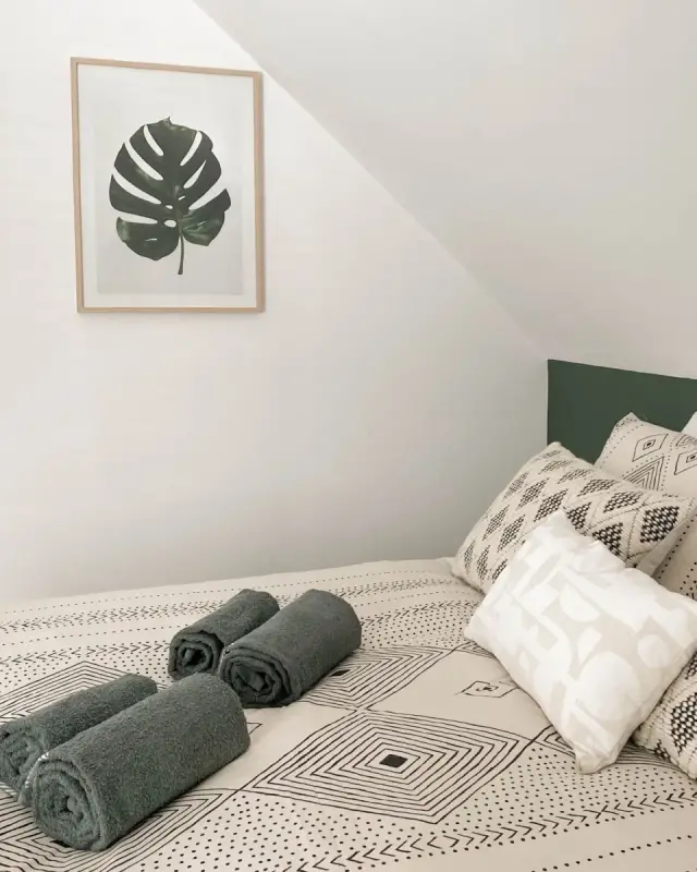 Chambre sous pente avec tête de lit vert foncé, linge de lit graphique noir et blanc et affiches végétales