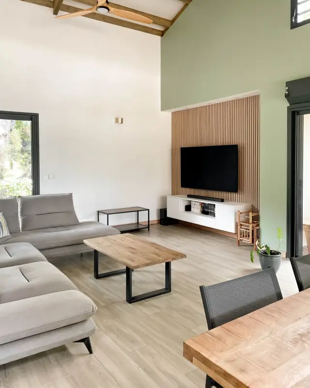 Table basse en bois massif sur piètement noir devant un meuble TV blanc suspendu et un mur vert sauge