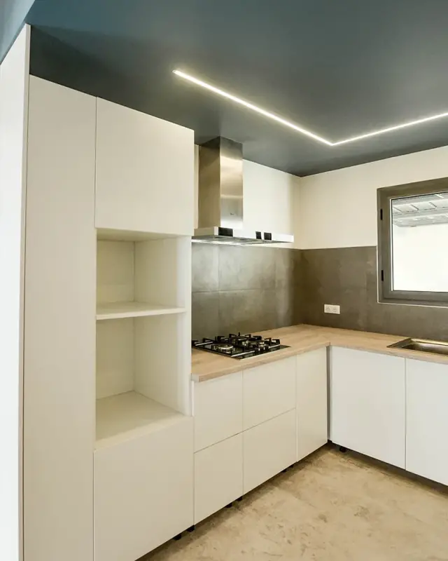 Cuisine blanche sans poignées avec plan de travail bois et plafond bleu nuit traversé d’un ruban lumineux