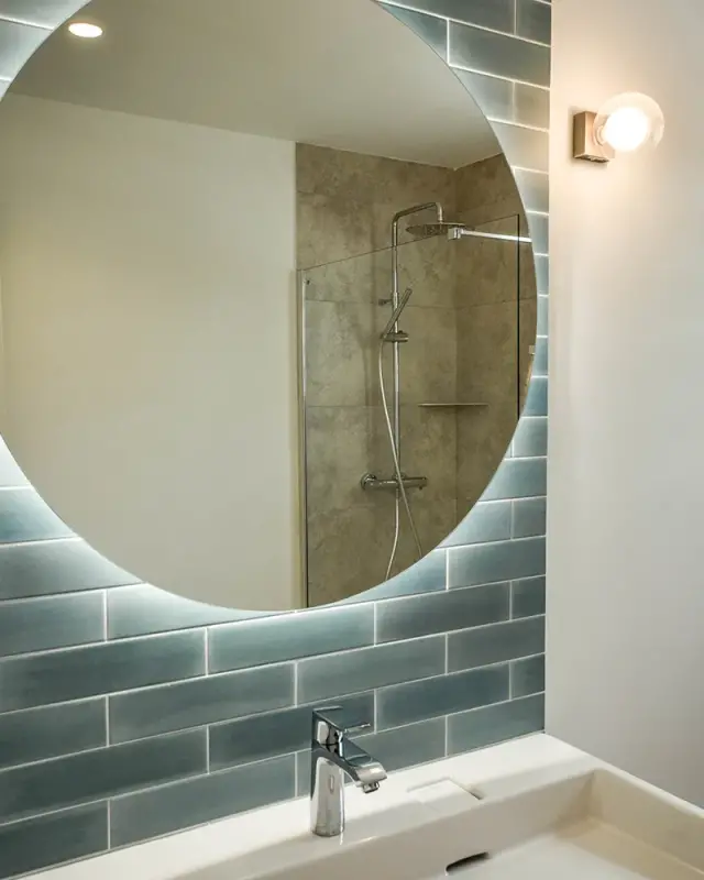 Miroir rond rétroéclairé sur faïence bleu-gris allongée au-dessus d’un plan vasque blanc