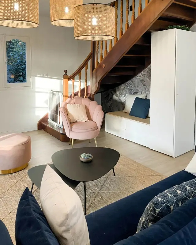 Banquette avec rangements sous un escalier en bois, papier peint tropical gris et fauteuil coquillage rose