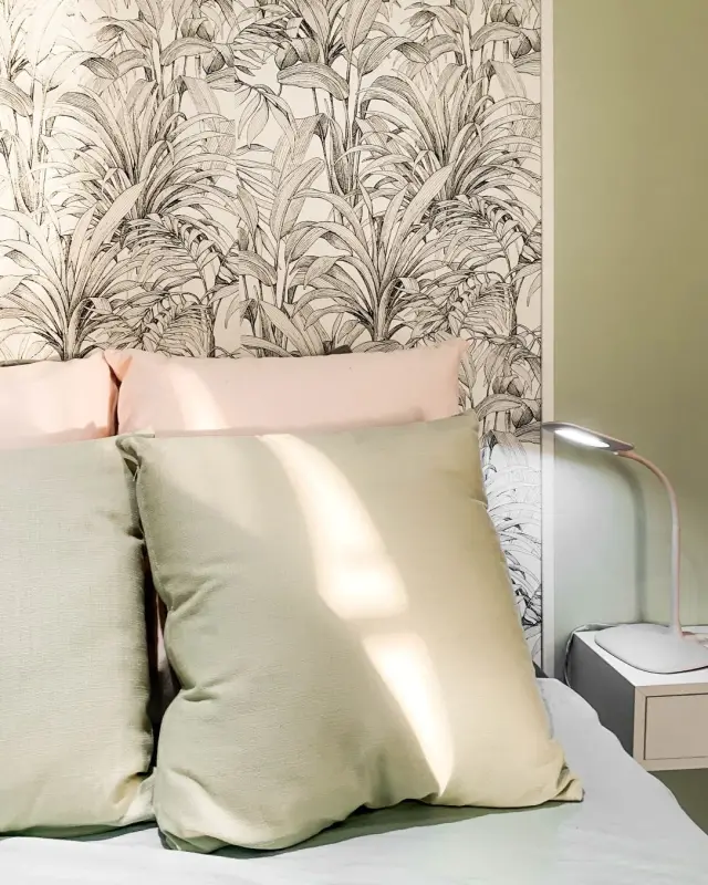 Coussins vert sauge et rose poudré devant un papier peint à palmes noir et blanc