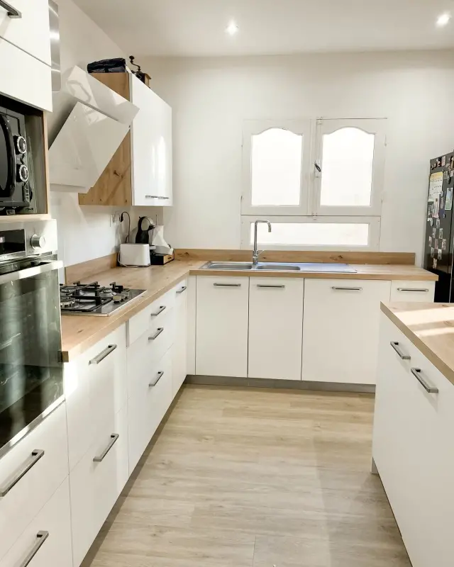 Cuisine blanche en U avec plan de travail effet chêne, plaque de cuisson et fenêtres cintrées