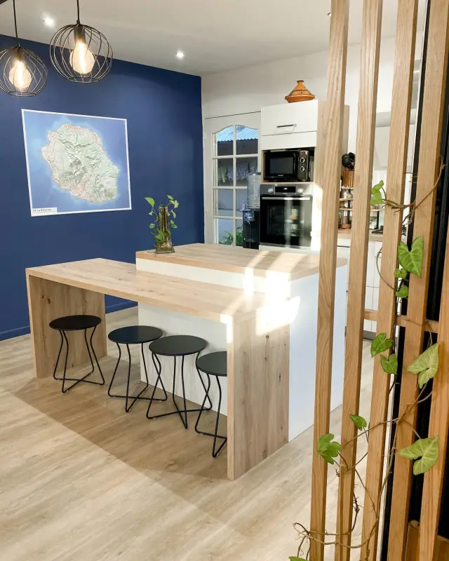 Îlot en bois à deux hauteurs avec tabourets noirs devant un mur bleu nuit orné d’une carte de La Réunion