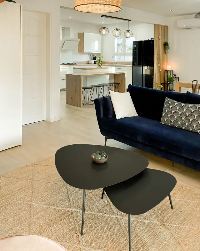 Tables basses gigognes noires sur tapis en jute, canapé bleu nuit et suspension en cannage