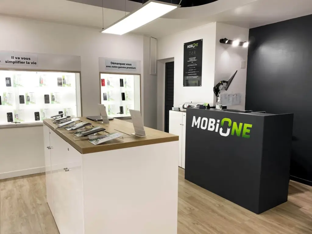 Boutique MobiOne modernisée à Saint-Pierre avec îlot blanc au plateau chêne, vitrines rétroéclairées et comptoir de caisse anthracite au logo vert