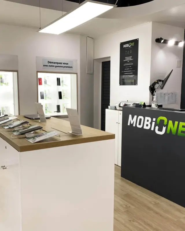 Boutique MobiOne modernisée à Saint-Pierre avec îlot blanc au plateau chêne, vitrines rétroéclairées et comptoir de caisse anthracite au logo vert
