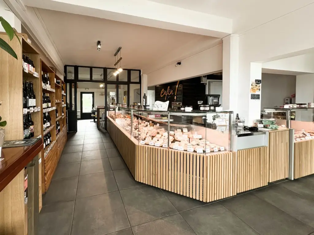 Intérieur de la fromagerie Enfin ! Le Fromager au Tampon avec vitrine à pans coupés habillée de chêne, rayonnages de vins et logo doré