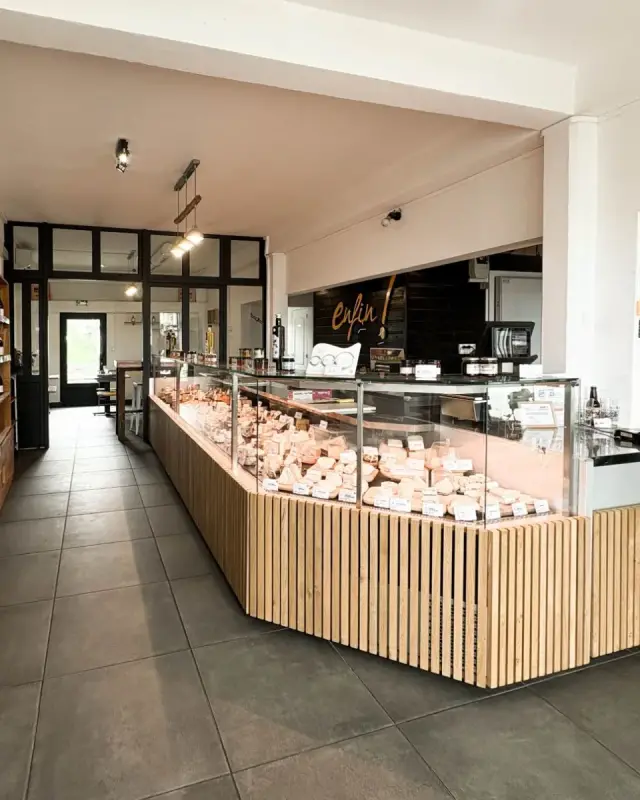Intérieur de la fromagerie Enfin ! Le Fromager au Tampon avec vitrine à pans coupés habillée de chêne, rayonnages de vins et logo doré