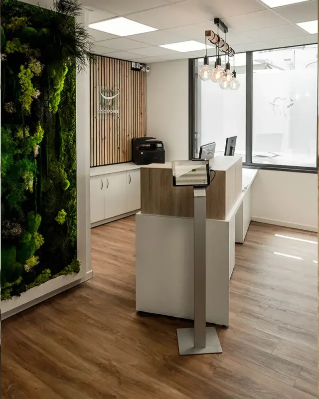 Accueil du cabinet dentaire Les Citadines à Saint-Pierre avec mur végétal, banque d’accueil blanche et panneau en bois
