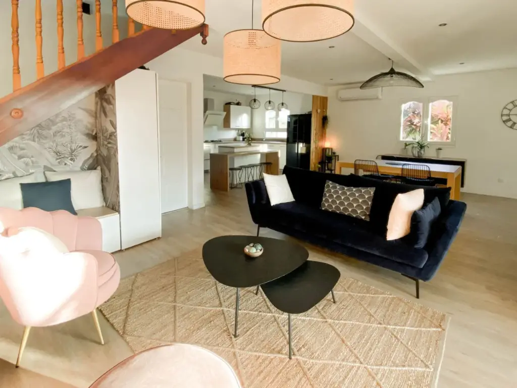 Pièce de vie d’une maison familiale rénovée à Saint-Pierre avec canapé en velours bleu nuit, fauteuil rose et cuisine ouverte