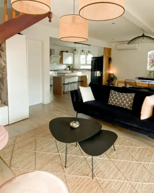 Pièce de vie d’une maison familiale rénovée à Saint-Pierre avec canapé en velours bleu nuit, fauteuil rose et cuisine ouverte