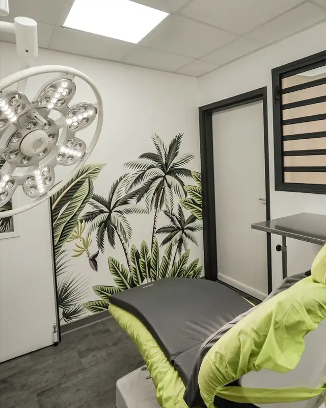 Salle de soins dentaires avec fauteuil vert anis, éclairage opératoire et papier peint tropical