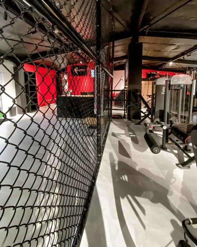 Cloison en grillage noir séparant l’accueil rouge de la zone de musculation sous un plafond noir