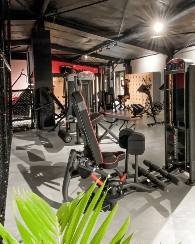 Zone de musculation guidée avec machines noires et rouges, cloison en grillage et casiers en bois clair